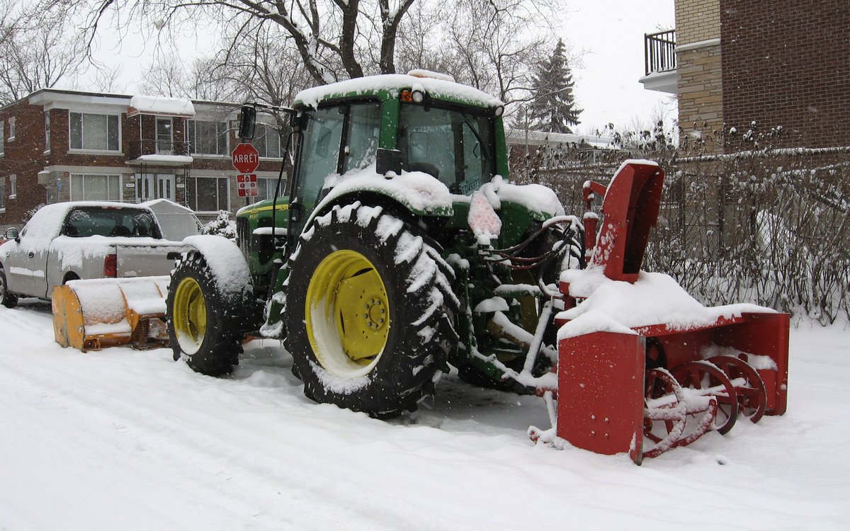 Tracteur John Deere avec souffleuse industrielle en action dans une cour résidentielle